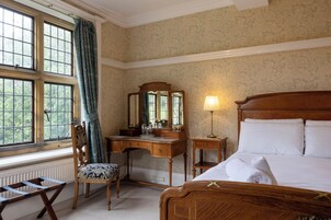 A hotel room with a wooden bed, a desk with a mirror, a chair, and a window with curtains.
