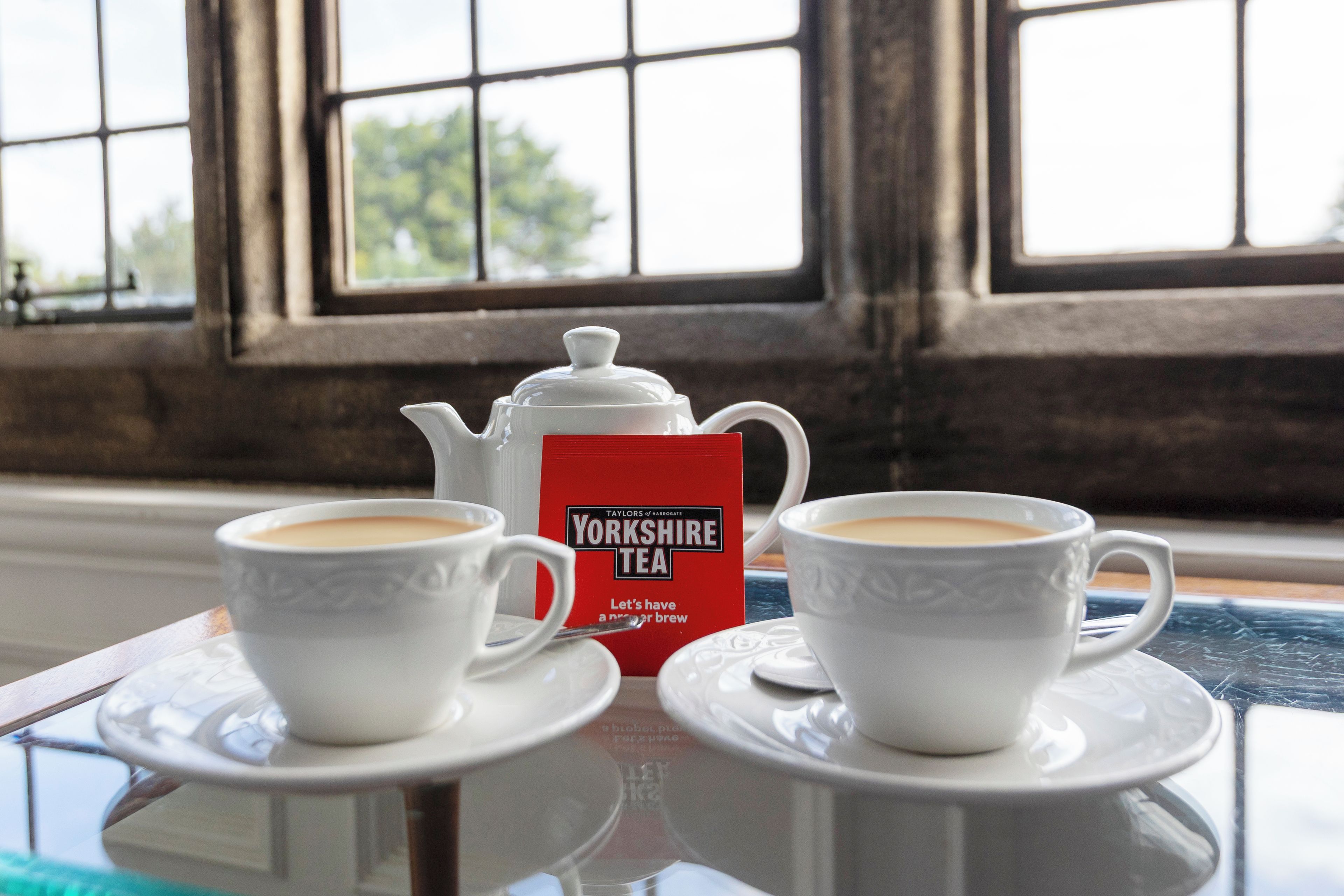 Two cups of tea on a table with a teapot and a red box of Yorkshire Tea.