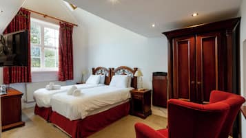 A hotel room with two beds, a red chair, a wardrobe, and a television.
