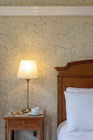 A neatly made bed with white linens, a wooden nightstand with a lamp, a cup, and glasses beside it.