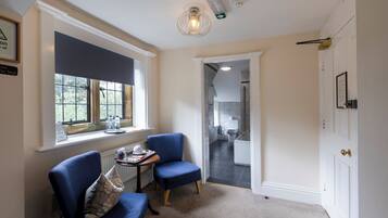 A room with two blue armchairs, a small table with a tray, a window with curtains, and a door leading to another room.