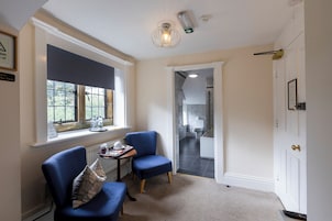 Una habitación con dos sillones azules, una mesita con bandeja, una ventana con cortinas y una puerta que da a otra habitación.