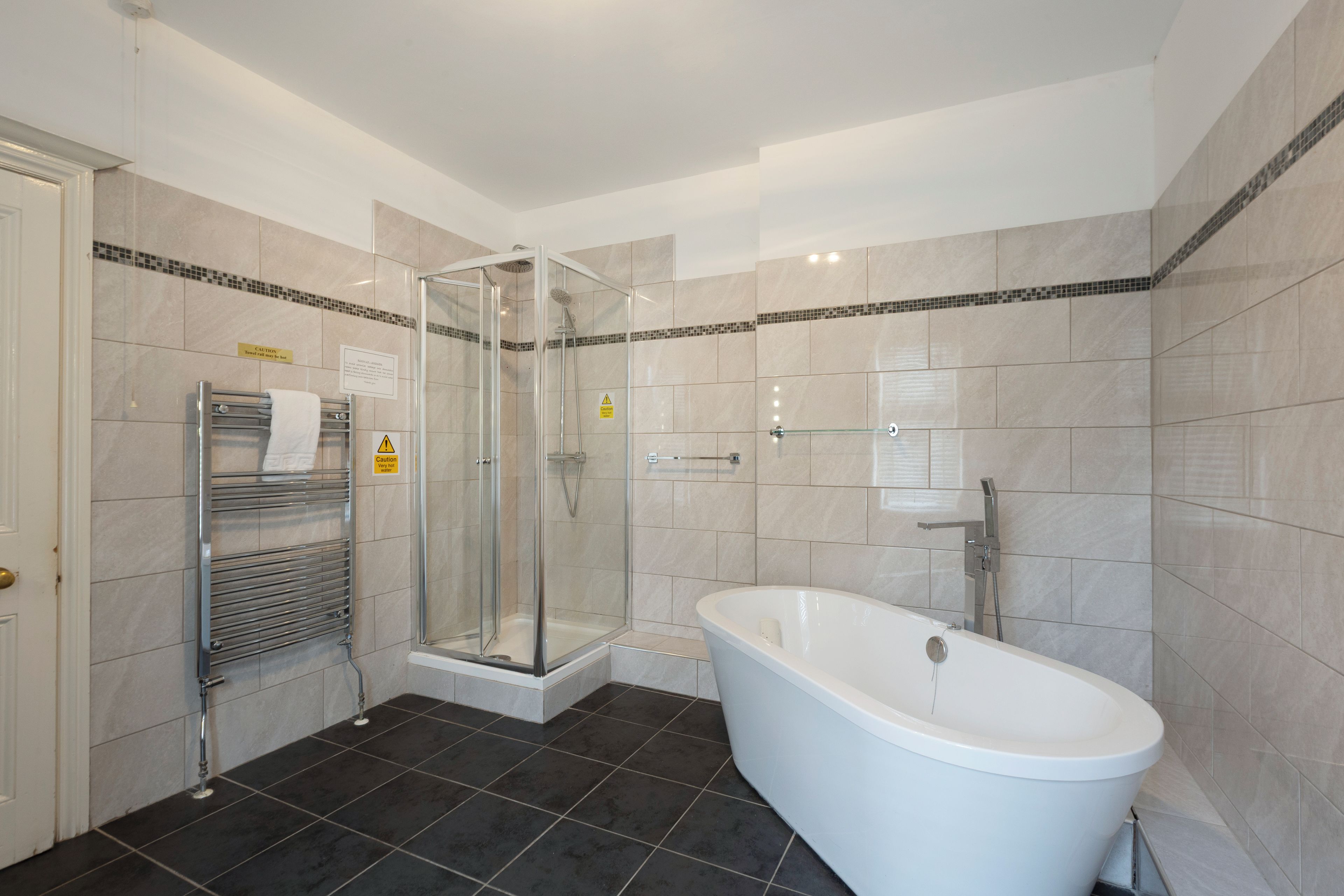 Un baño moderno con ducha envuelta en vidrio, una bañera independiente y un perchero para toallas.
