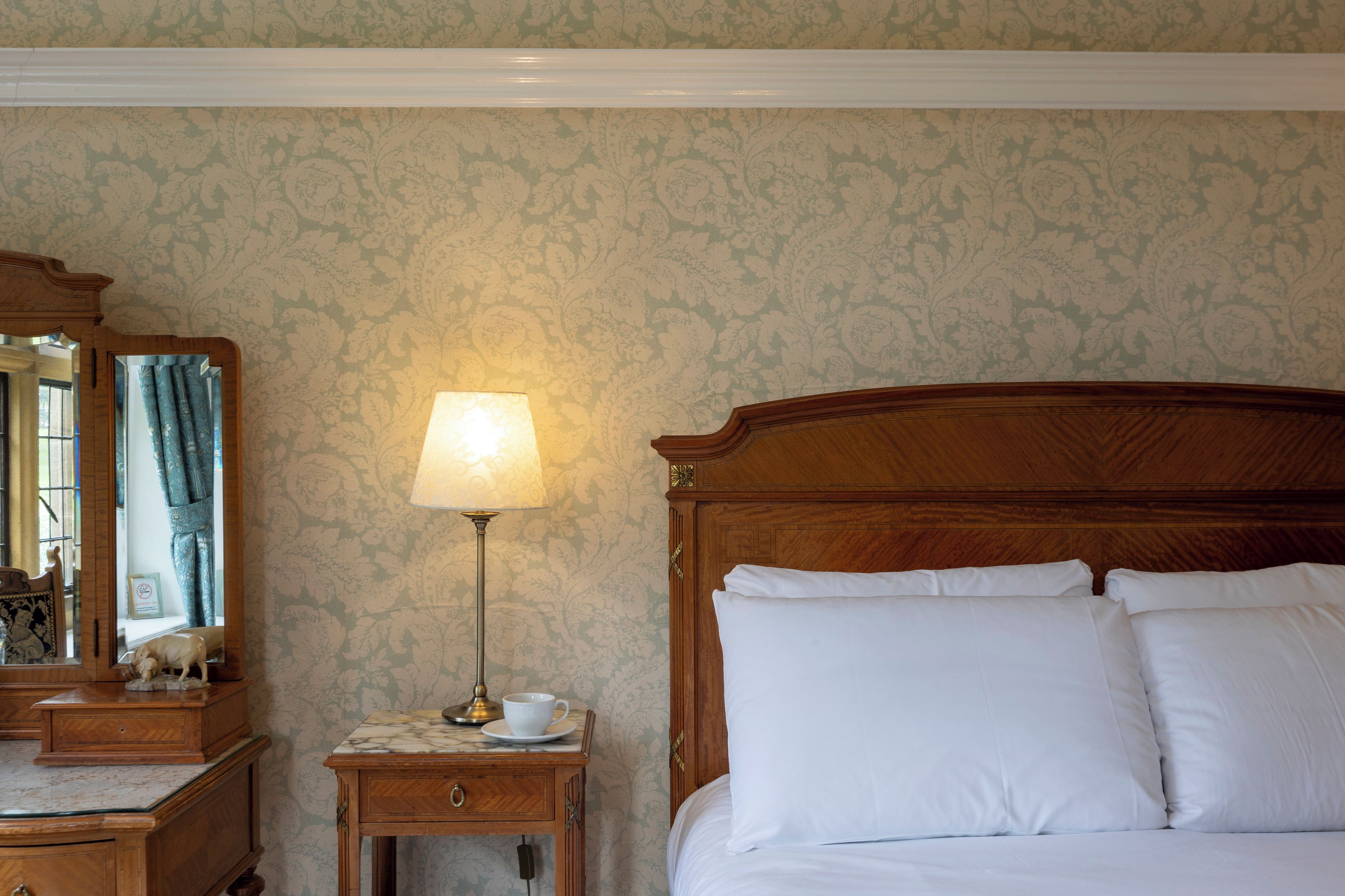 Une chambre d’hôtel avec un lit en bois, une table de chevet avec une lampe, un miroir et une commode.