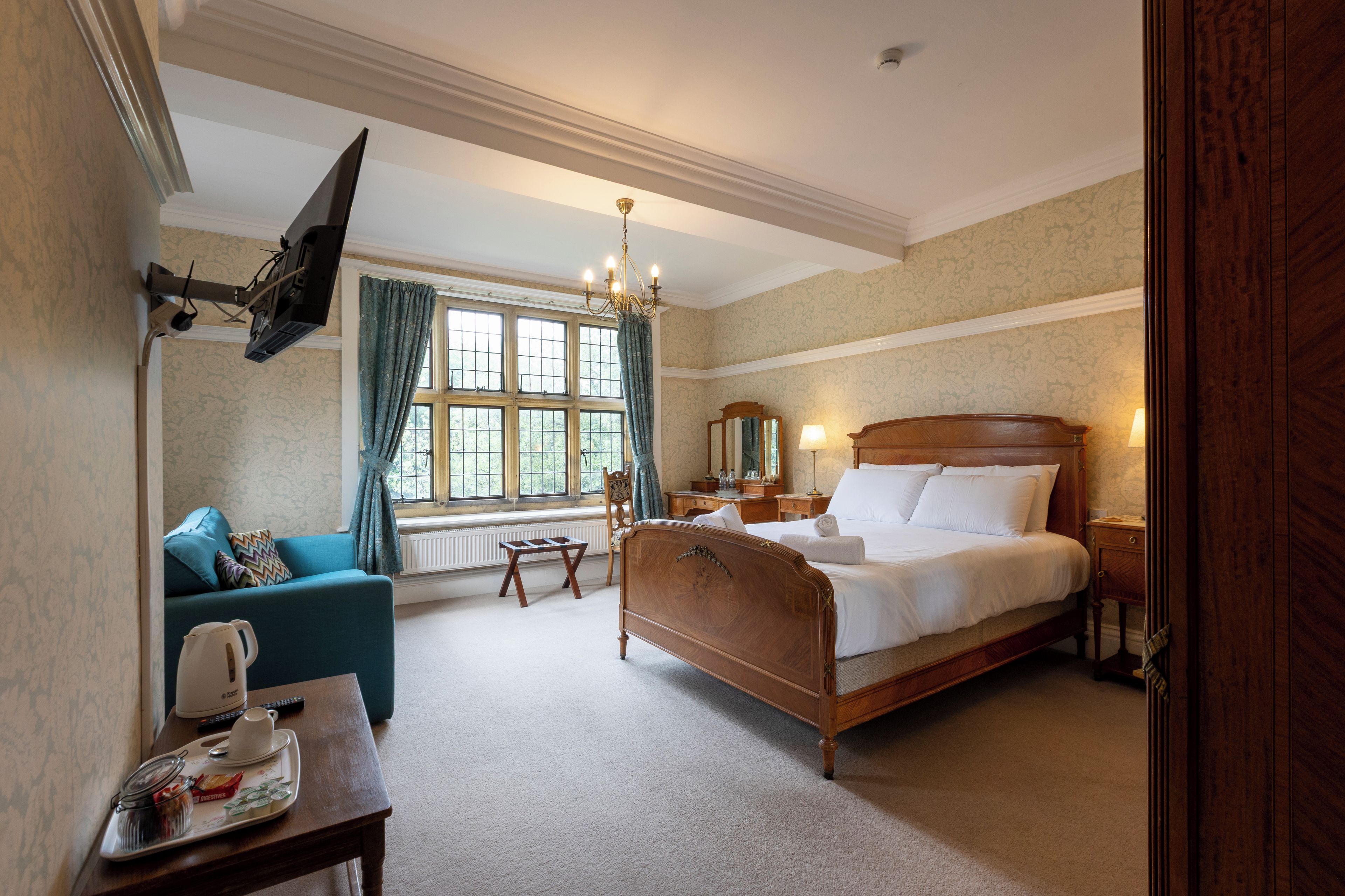 A hotel room with a large bed, a sitting area with a sofa, a small table with a tray, a window with curtains, and a chandelier.