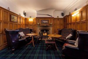 A traditional room with leather armchairs, a fireplace, and a plaid carpet.