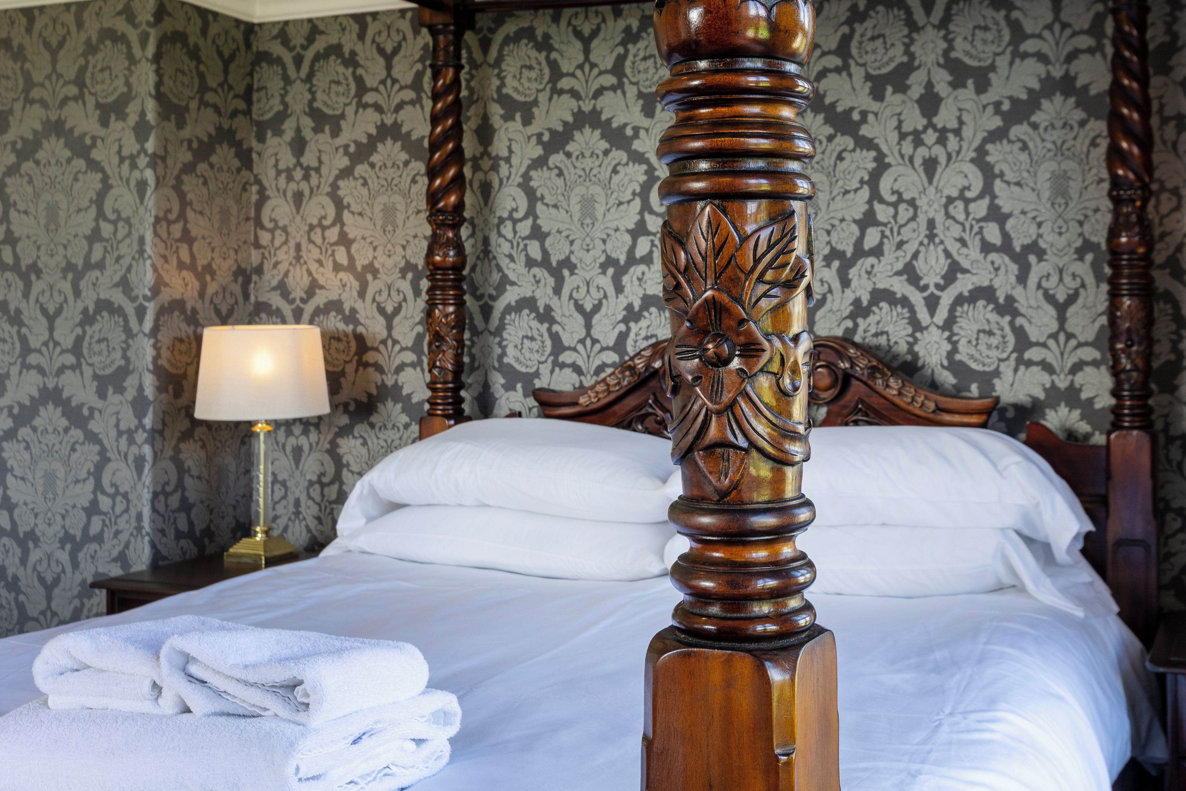 Un lit bien fait, avec du linge de lit blanc, une tête de lit en bois ornée de motifs complexes et une lampe sur une table de chevet.