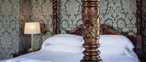A neatly made bed with white linens, a wooden headboard with intricate carvings, and a lamp on a bedside table.