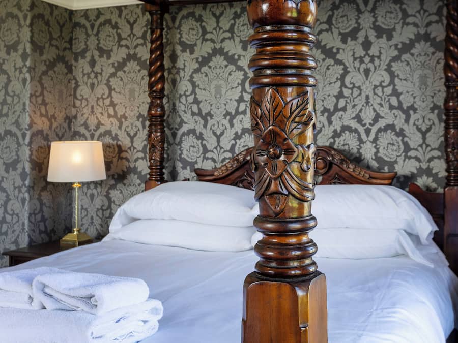 A neatly made bed with white linens, a wooden headboard with intricate carvings, and a lamp on a bedside table.