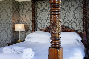 A neatly made bed with white linens, a wooden headboard with intricate carvings, and a lamp on a bedside table.