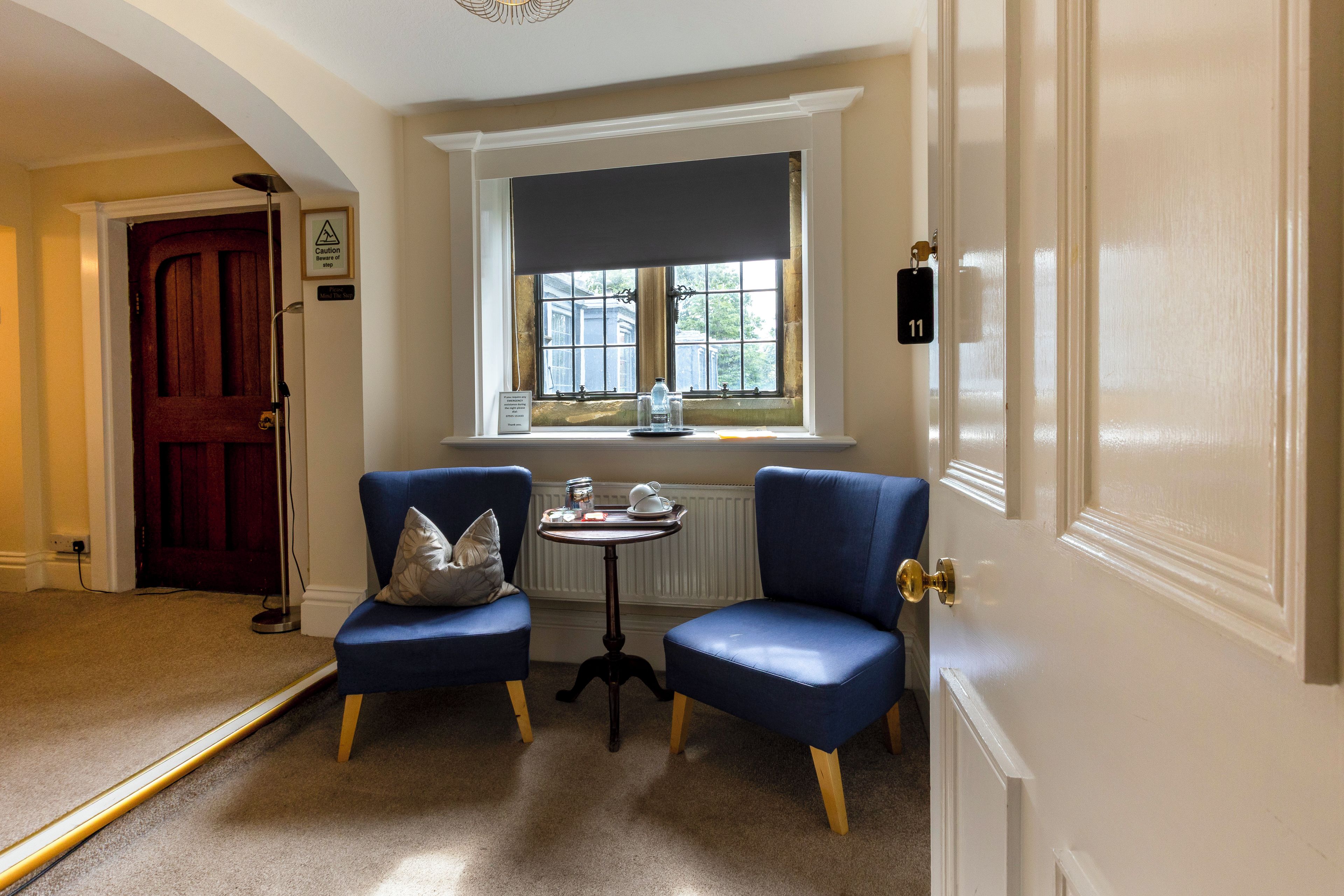 Une pièce avec deux chaises bleues, une petite table avec un plateau, une fenêtre donnant sur un paysage et une porte avec une plaque numérotée.