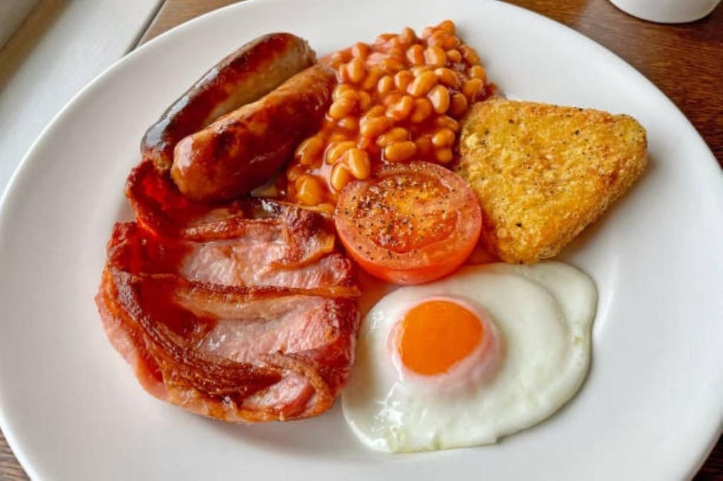 A plate with bacon, sausages, baked beans, a fried egg, and a slice of toast.