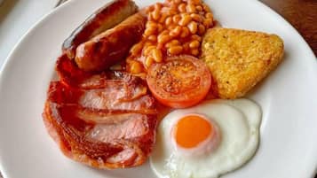 A plate with bacon, sausages, baked beans, a fried egg, and a slice of toast.