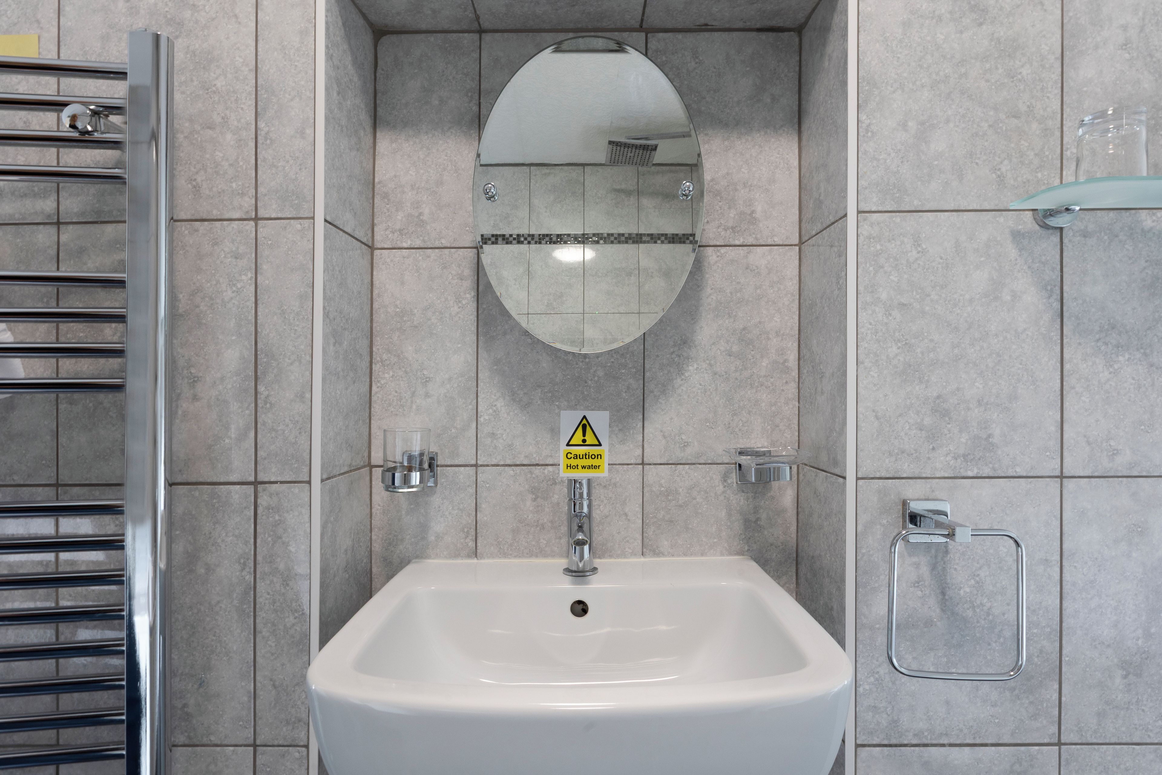 A bathroom with a white sink, a mirror, and a caution sign for hot water.