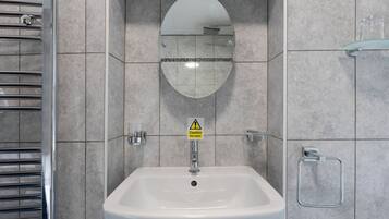 A bathroom with a white sink, a mirror, and a caution sign for hot water.