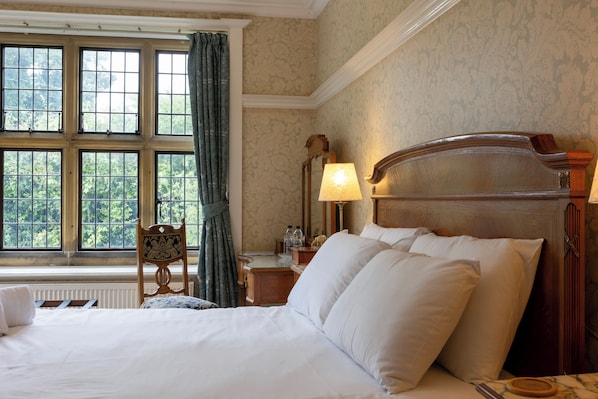 A hotel room with a large bed, a nightstand, a lamp, a chair, and a window with curtains.