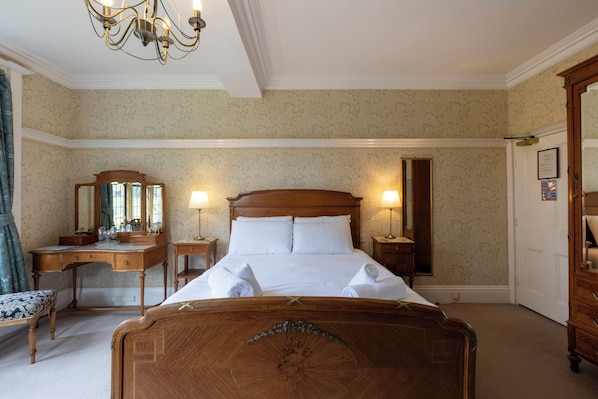 Una habitación de hotel con una cama grande, un aparador de madera, un escritorio con espejo y una araña.