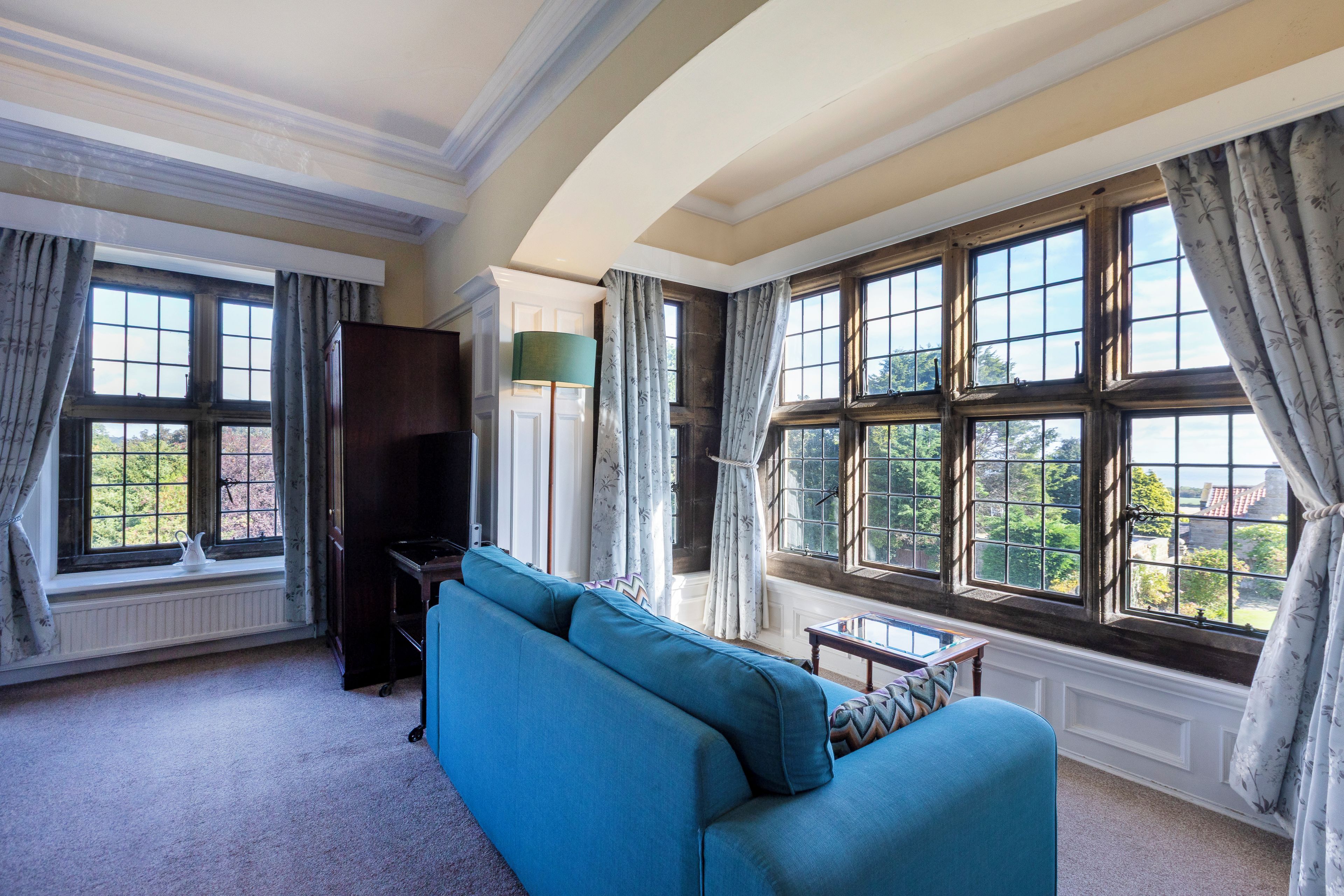 A spacious room with a large window, a blue sofa, and a television.