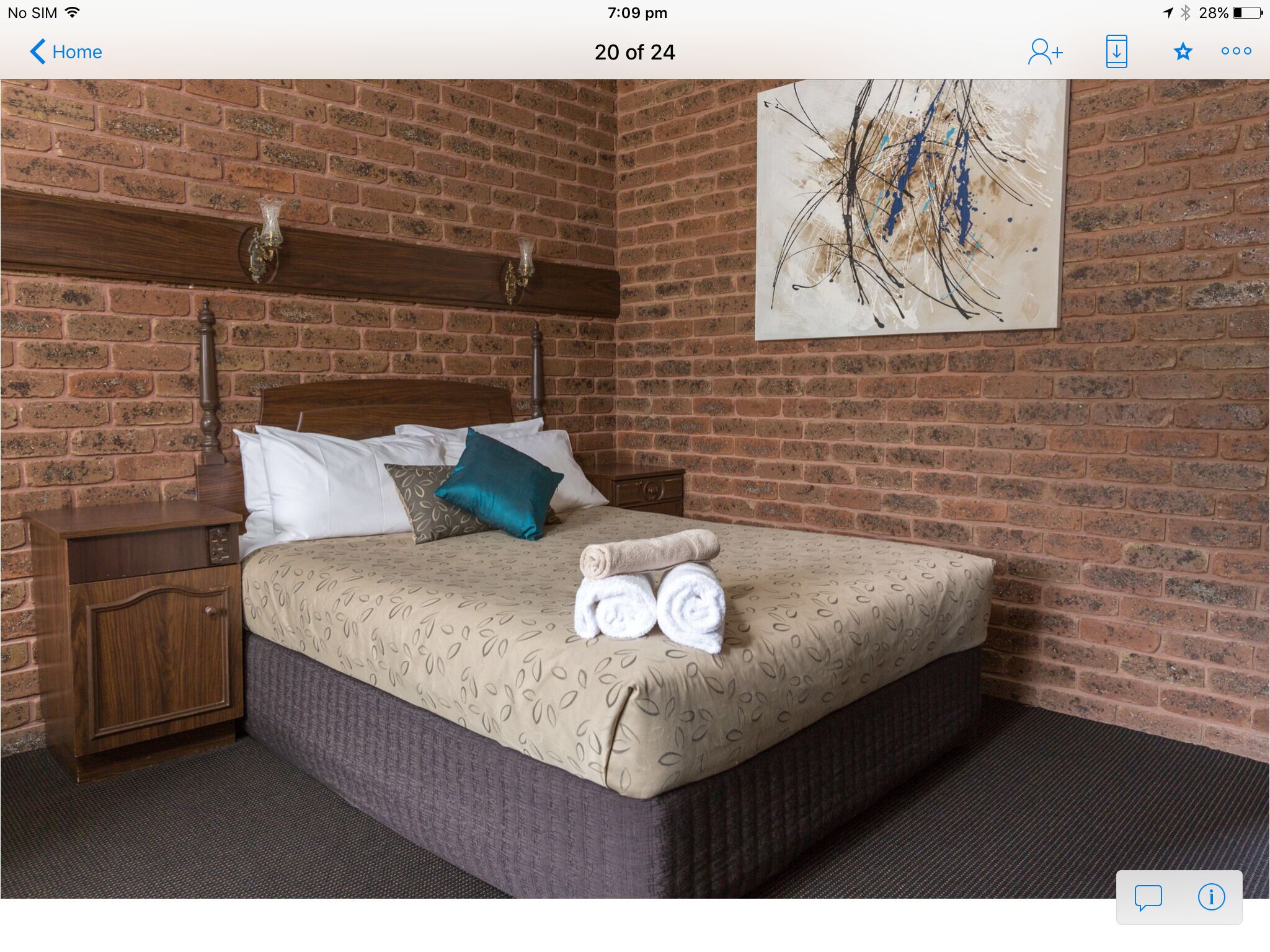 Un dormitorio con pared de ladrillo, cabecera de madera, cama con ropa de cama estampada, mesita de noche y un cuadro.