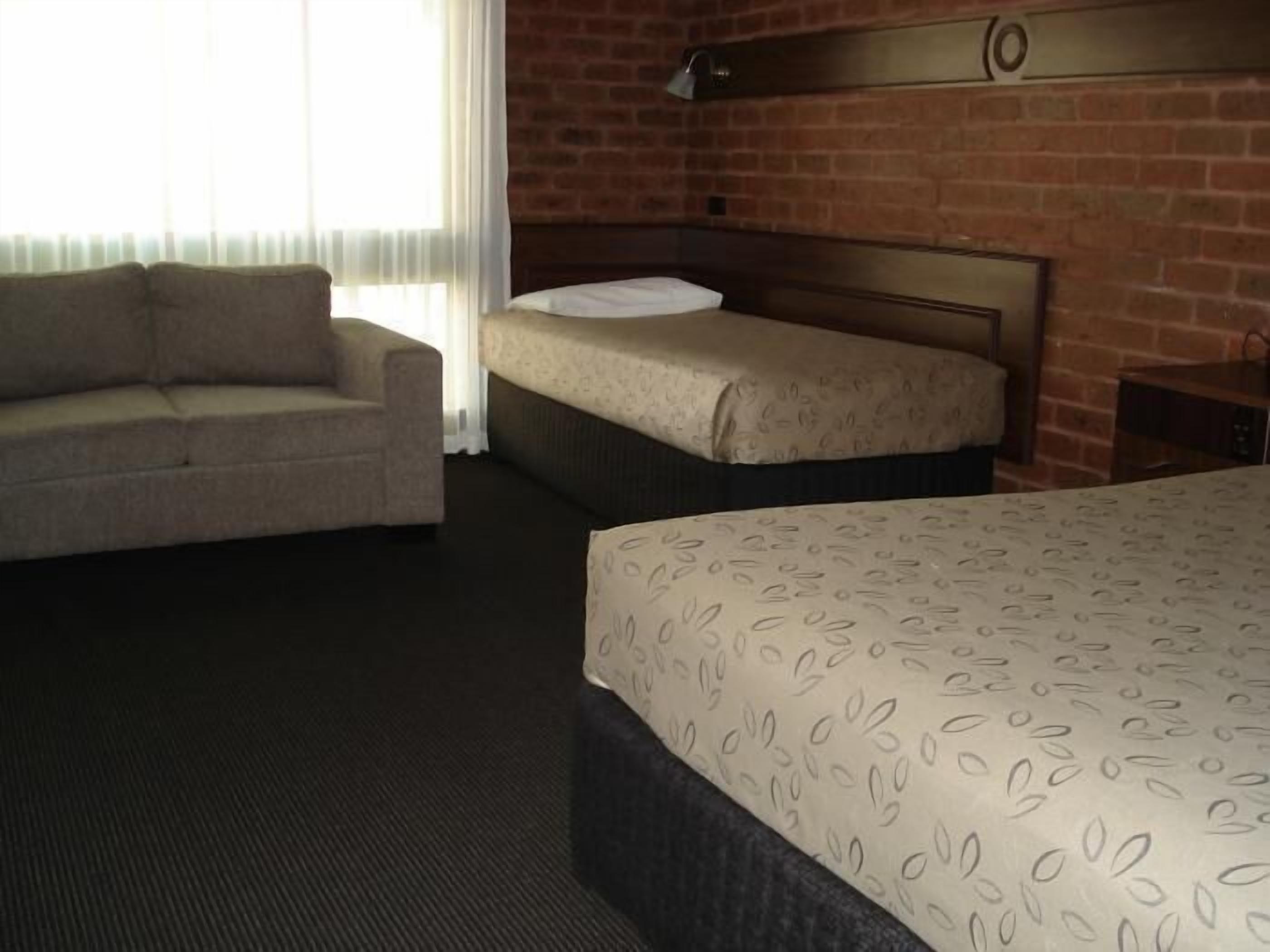 A hotel room with a large bed, a smaller bed, a sofa, and a brick wall.
