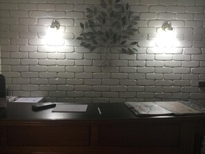 A room with a brick wall, two wall-mounted lights, a desk with papers, a pen, and a plant. - Albury Townhouse Motel (Albury)