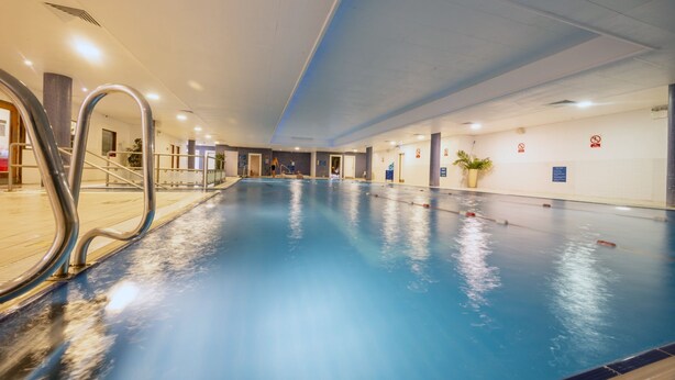 Una piscina interior con carriles delimitados, una barandilla de metal y suelo de baldosas.