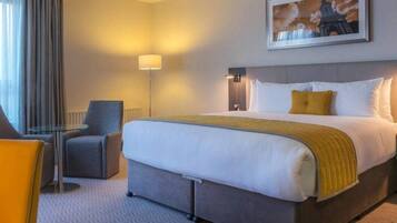 A hotel room with a bed, a desk, a chair, a lamp, and a coffee maker.