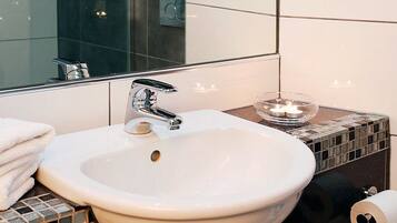 A bathroom with a white sink, a mirror, a towel stack, and a candle in a glass holder.