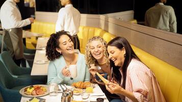 Un grupo de personas cenando en un restaurante con asientos tipo cabina amarillos y ambiente relajado.