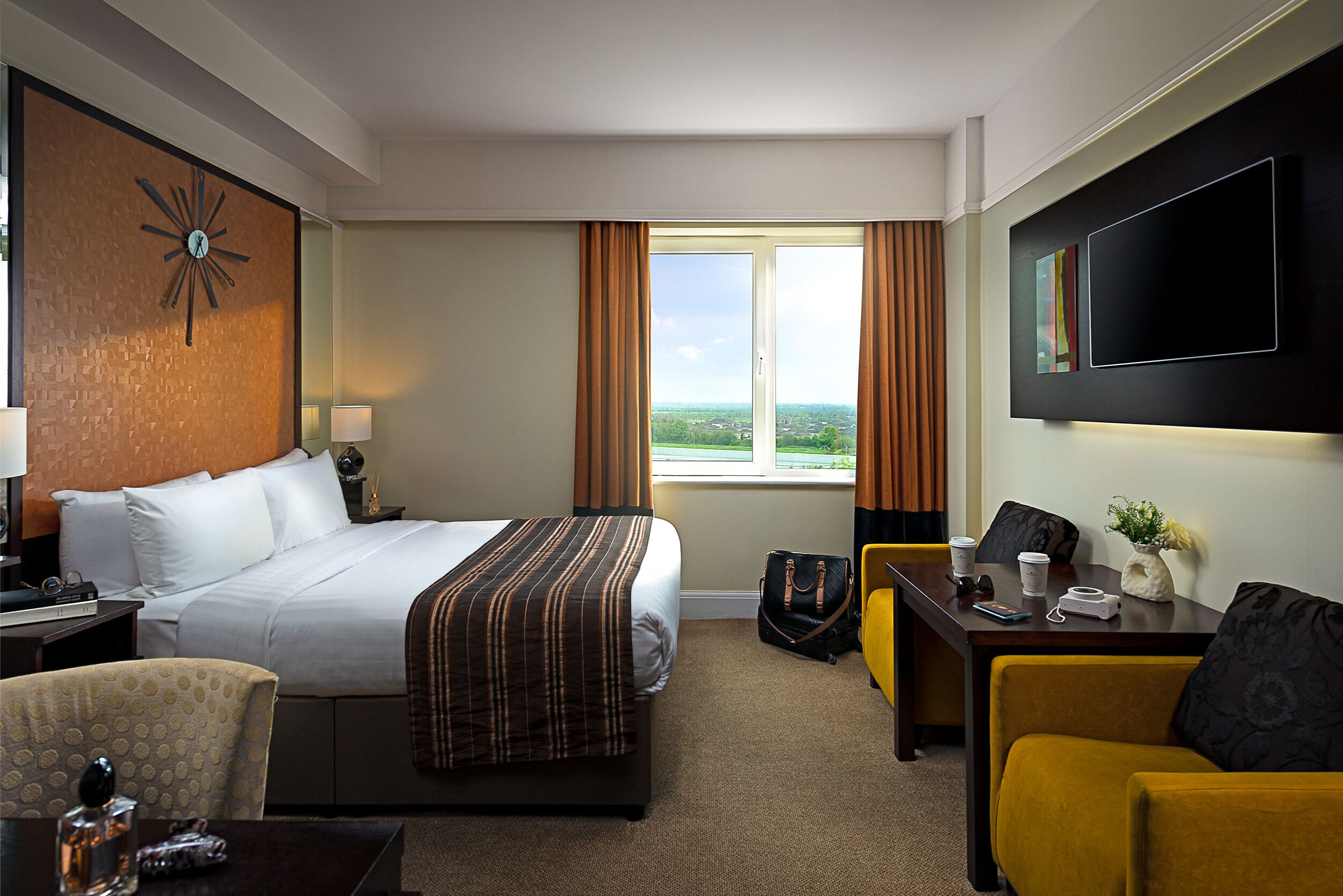 A hotel room with a bed, a desk, a chair, a TV, and a window with curtains.