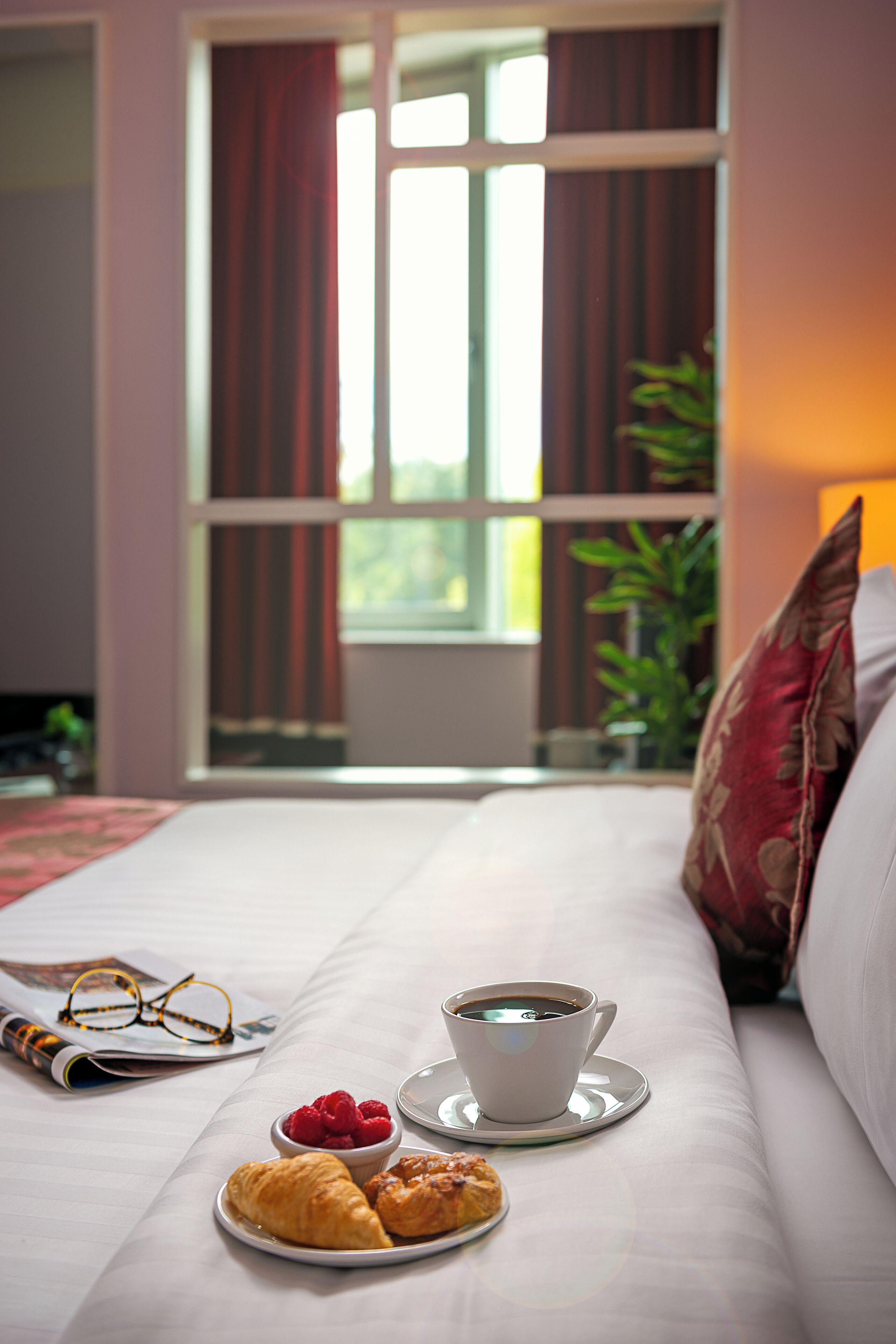 Een keurig opgemaakt bed met een kop koffie, croissants en een bord bessen.