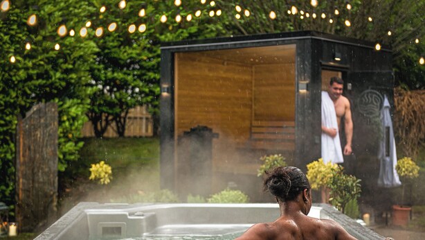 A hot tub with a person relaxing, surrounded by greenery and string lights.