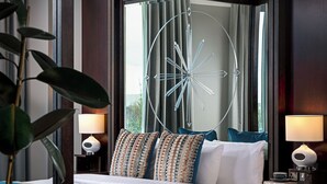 A modern hotel room with a large bed, a decorative ceiling light, and a view of the outdoors.