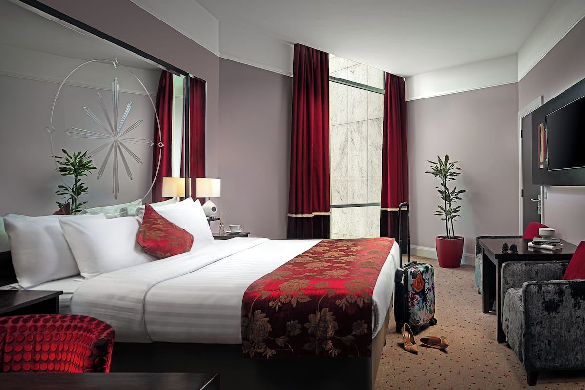 Een hotelkamer met een groot bed, een bureau, een stoel, een televisie en twee potplanten.