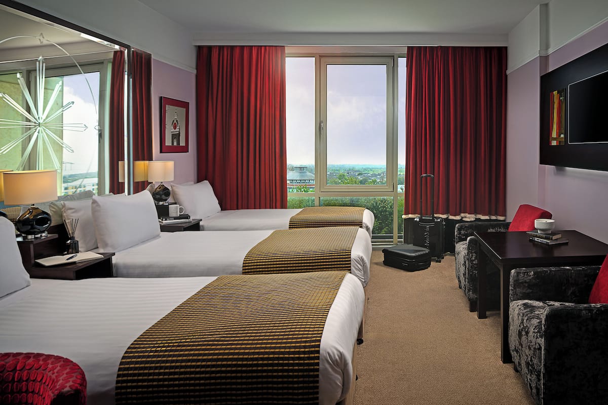 Een hotelkamer met twee bedden, een bureau, een stoel en een groot raam met uitzicht over de stad.