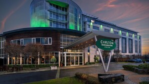 A modern hotel with a curved glass facade, a covered entrance, and a sign indicating it is the Carlton Blanchardstown.