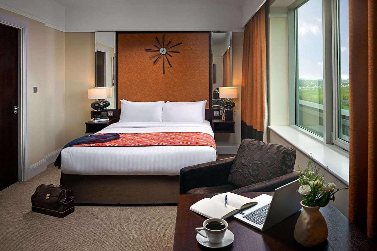 Een hotelkamer met een groot bed, een bureau met een laptop, een koffiekop en een bloemetjesvaas.