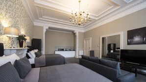 A spacious bedroom with a large bed, two sofas, a TV, and a chandelier. - Grosvenor Suites (Edinburgh)