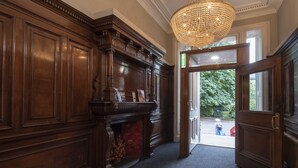 A grand hallway with a wooden panel wall, a chandelier, and a door leading outside. - Grosvenor Suites (Edinburgh)