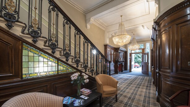 A grand staircase with ornate railings, a checkered floor, and a chandelier. - Grosvenor Suites (Edinburgh)
