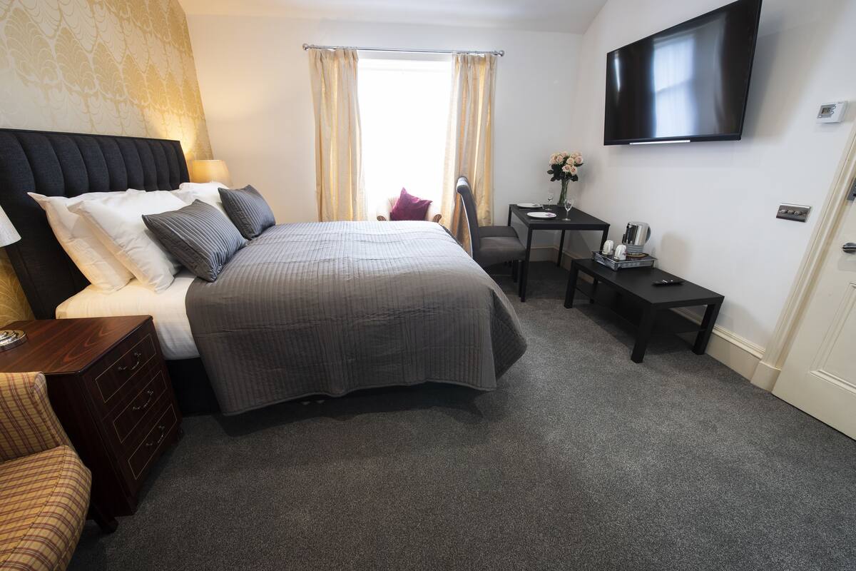 A hotel room with a large bed, a desk, a chair, a TV, and a window with curtains.