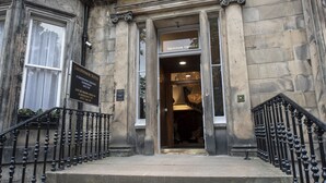 The entrance to Grosvenor Suites, Edinburgh, with a stone facade, black iron railings, and a sign indicating the suite number and contact information. - Grosvenor Suites (Edinburgh)
