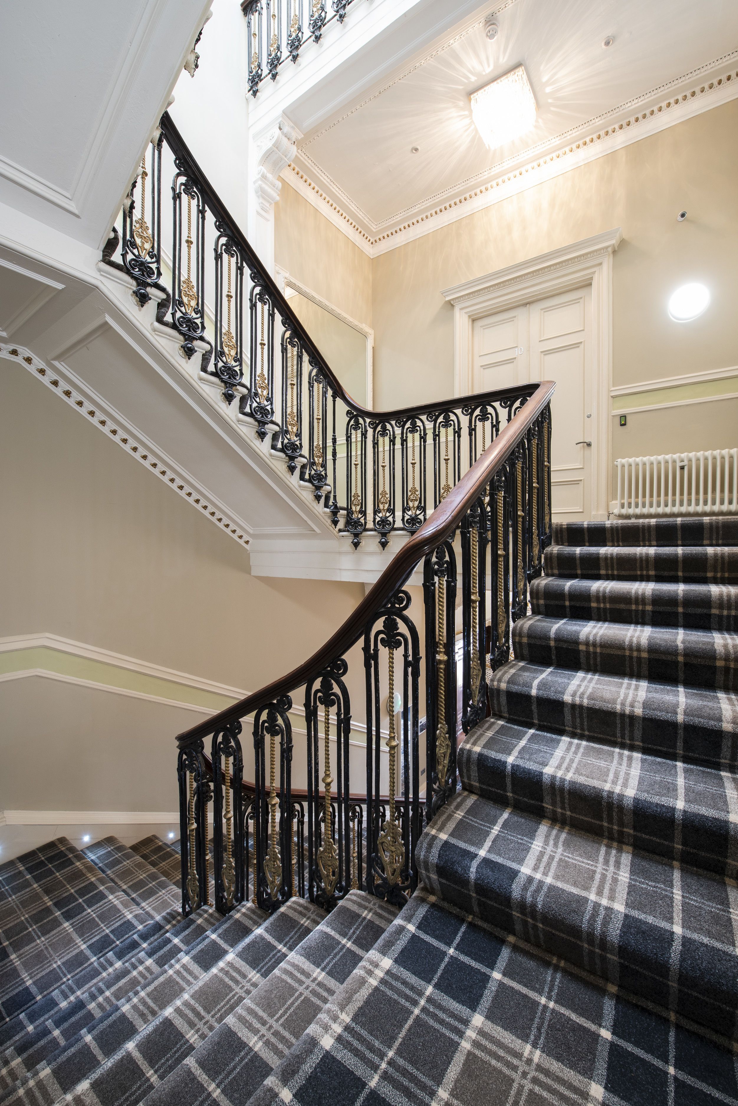 A grand staircase with ornate black iron railings and plaid carpeted steps.
