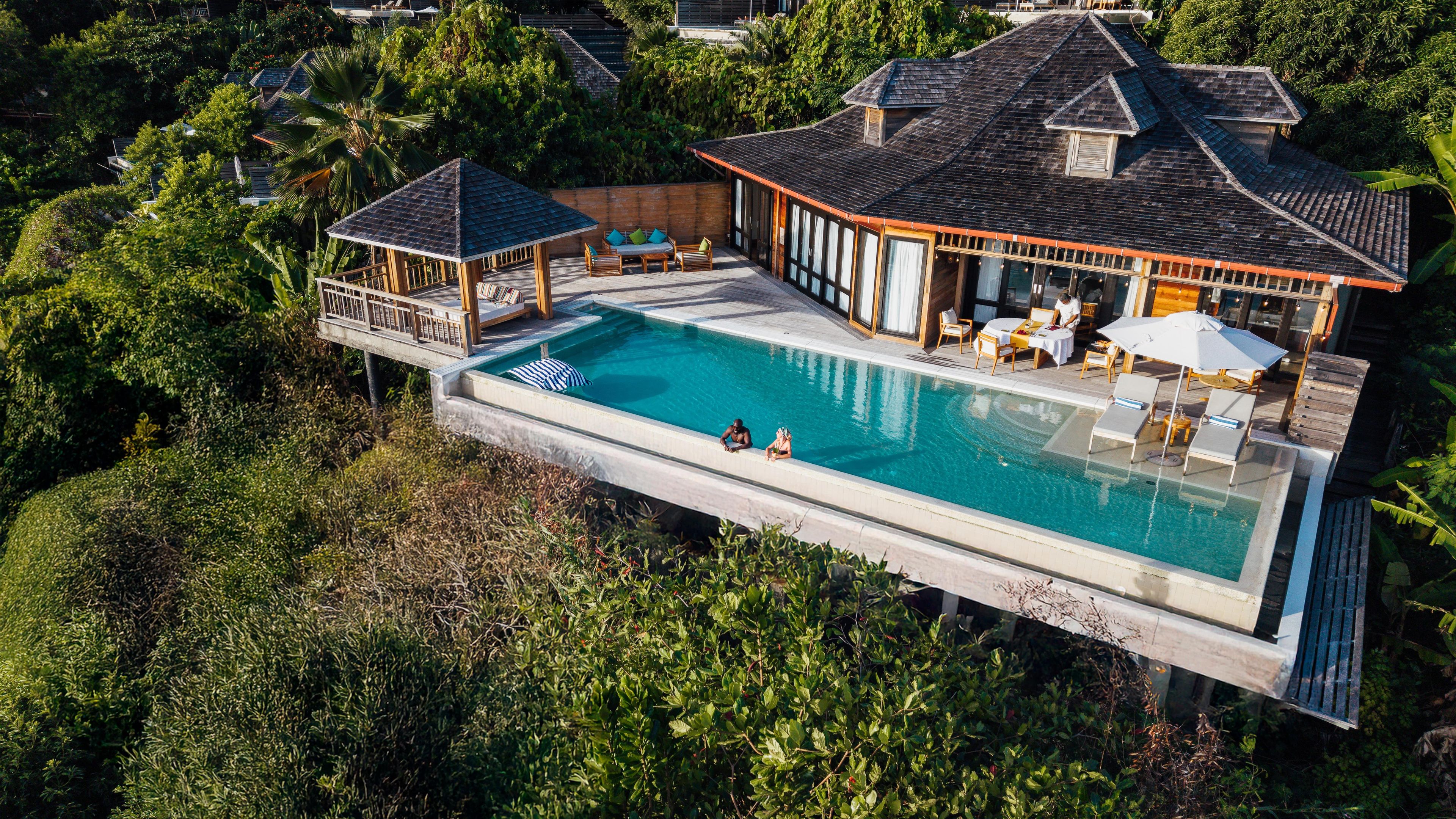 Una casa lujosa con una piscina grande, un porche cubierto y una terraza de madera.