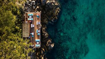 An aerial view of a wooden deck with multiple seating areas, surrounded by rocky terrain and dense vegetation.