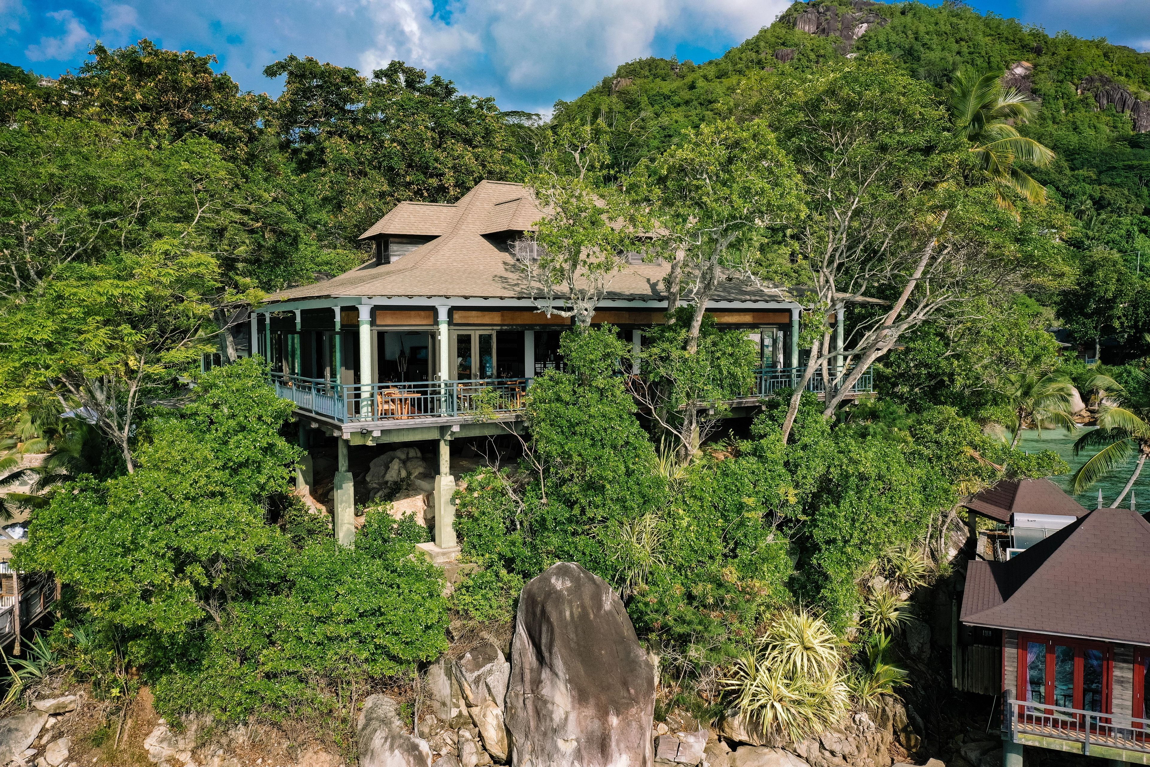 Una casa con balcón, rodeada de abundante vegetación y un paisaje rocoso.