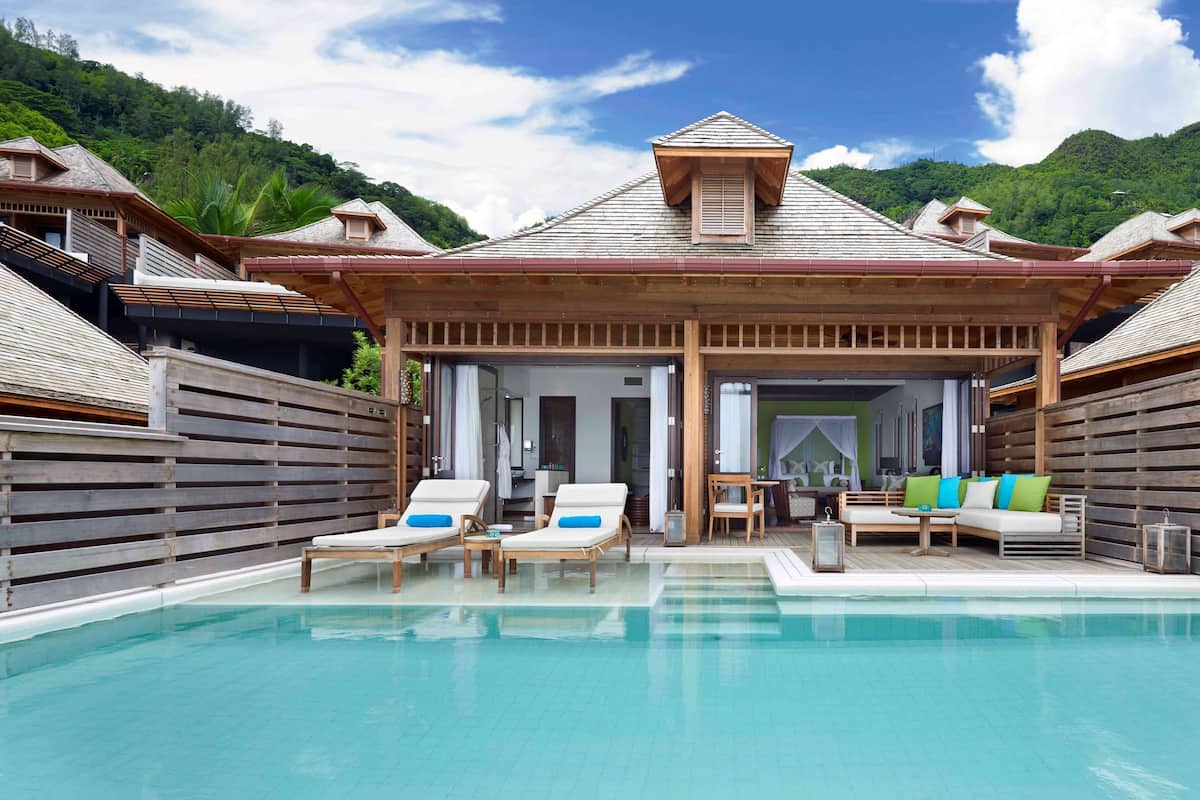 Ein Poolbereich mit Holzterrasse und Liegestühlen, umgeben von Holzhütten mit geneigten Dächern.