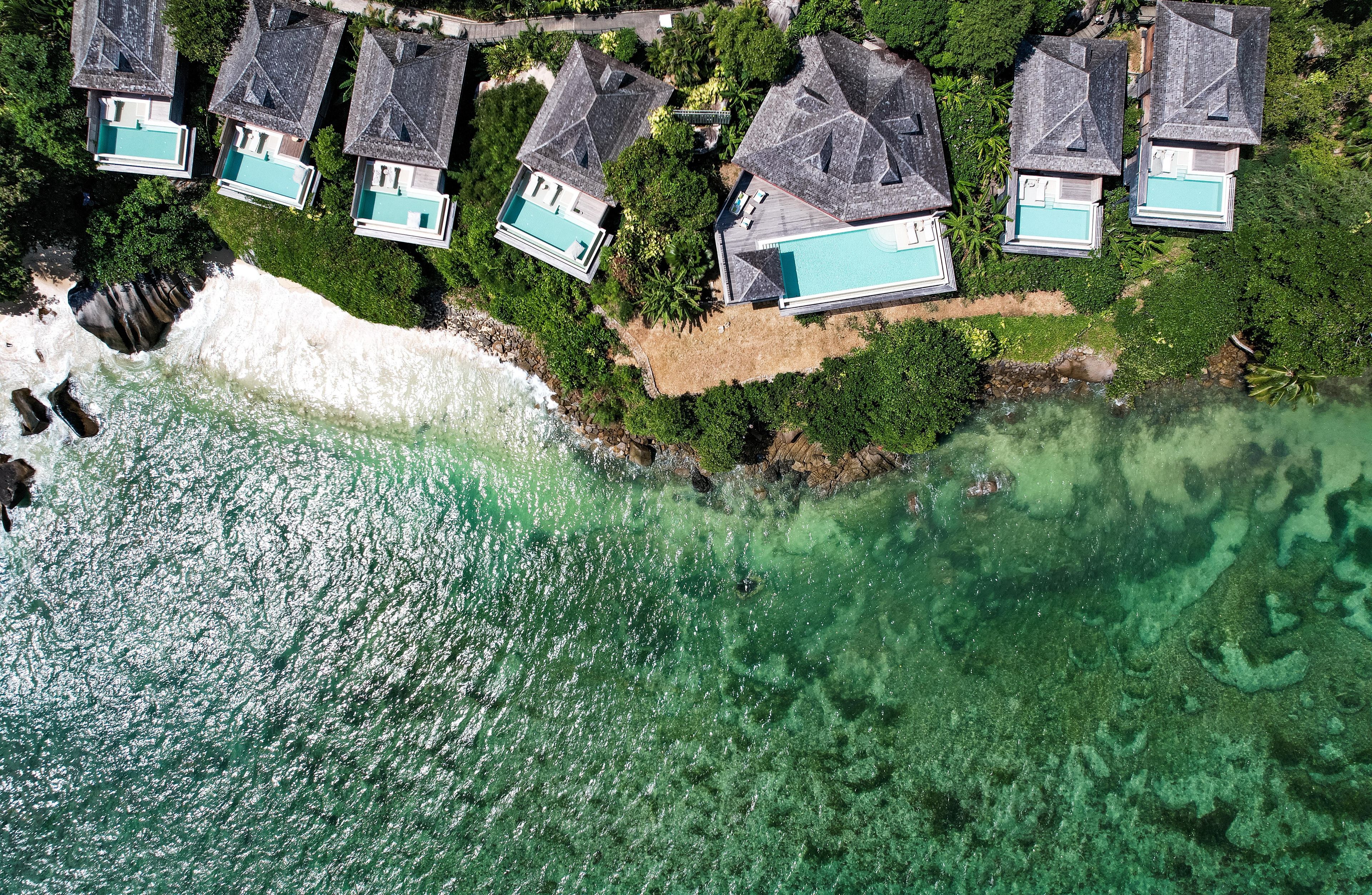 An aerial view of a coastal property with multiple houses, each featuring a swimming pool.