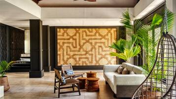 A spacious lobby with a high ceiling, a ceiling fan, a patterned wall, a sofa, a chair, and several potted plants.