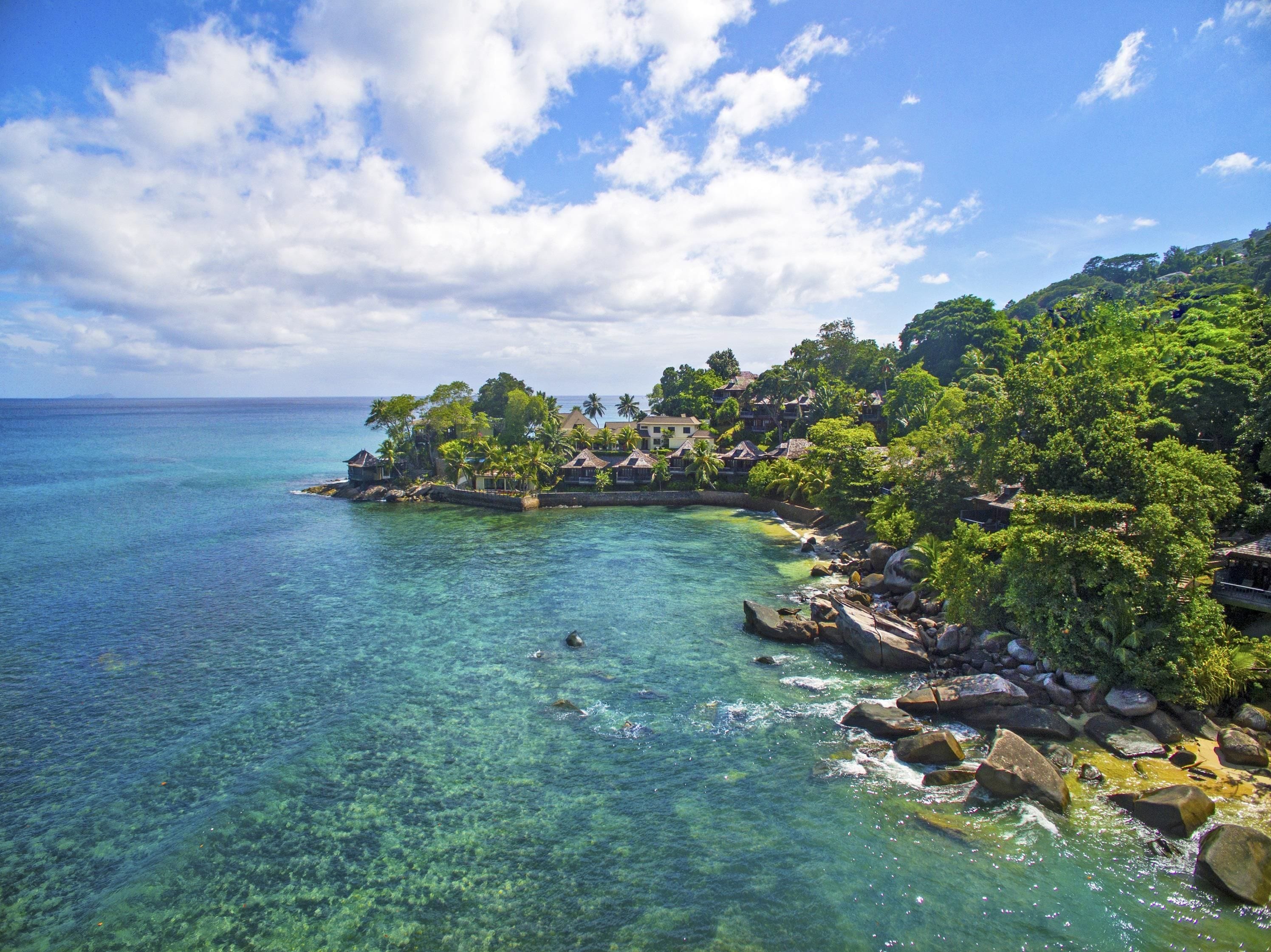 A coastal resort with clear turquoise waters, lush greenery, and traditional-style buildings.